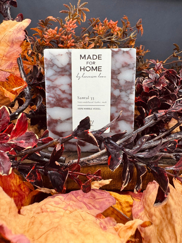 Candle packaging labeled 'Made for Home' surrounded by autumn leaves and branches.